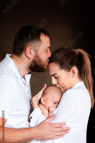Family of three holding newborn baby, hugging and kissing each other.