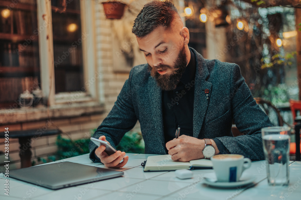 Businessman using a smartphone and a notebook in a coffee shop Businessman using a smartphone and a notebook in a coffee shop