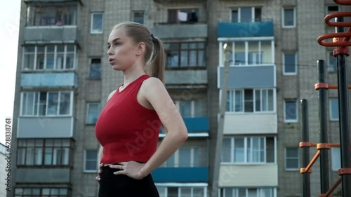young fit blond busty woman with ponytail in red top exhales at sports ground