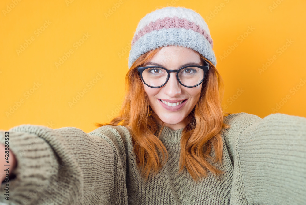 Close-up smile woman takes photo of himself with her smartphone. Selfie, isolated on yellow background. Focus on face