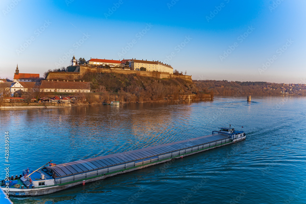View on cargo ship passing by Petrovaradin fortress over Danube river in Novi Sad, Serbia