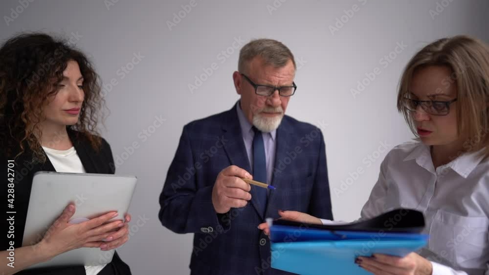 Mature businessman with a business suit signs the urgent papers that his secret brought him. Portrait of two business women and their boss Mature businessman with a business suit signs the urgent papers that his secret brought him. Portrait of two business women and their boss