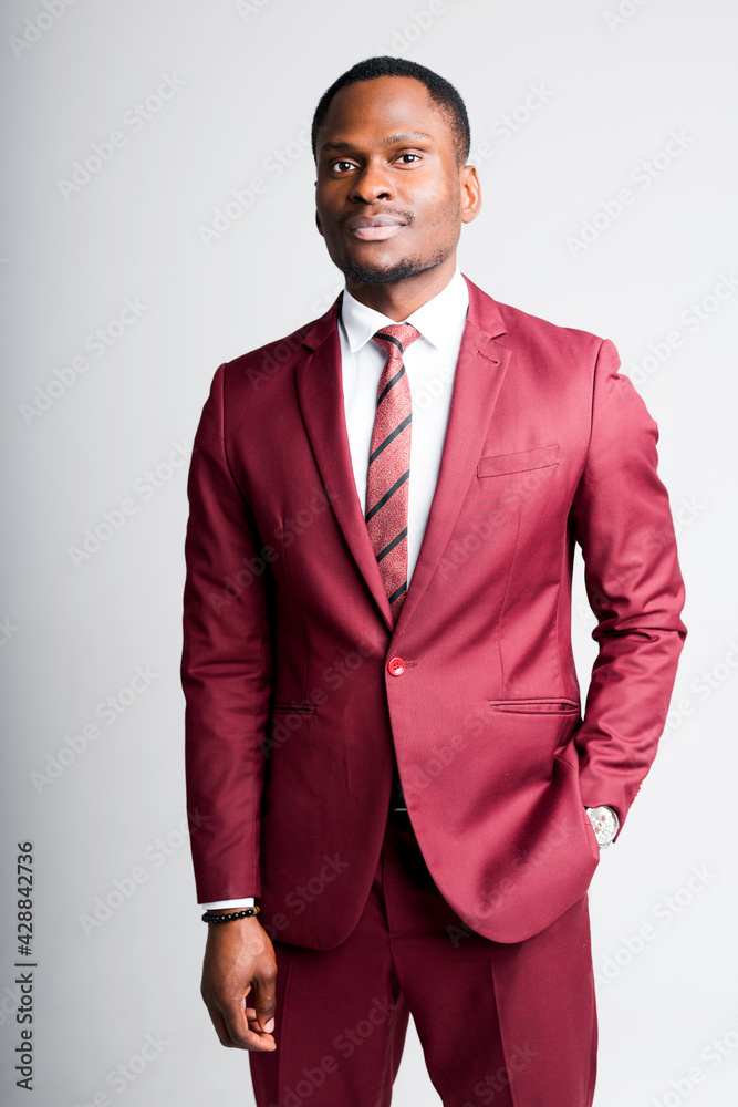 Fototapeta premium Serious manager from nigeria in suit with hand in pocket looking at camera while standing on white background