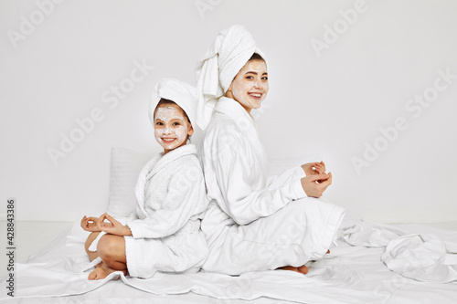 mother and daughter are sitting with towels on head and facial mask.