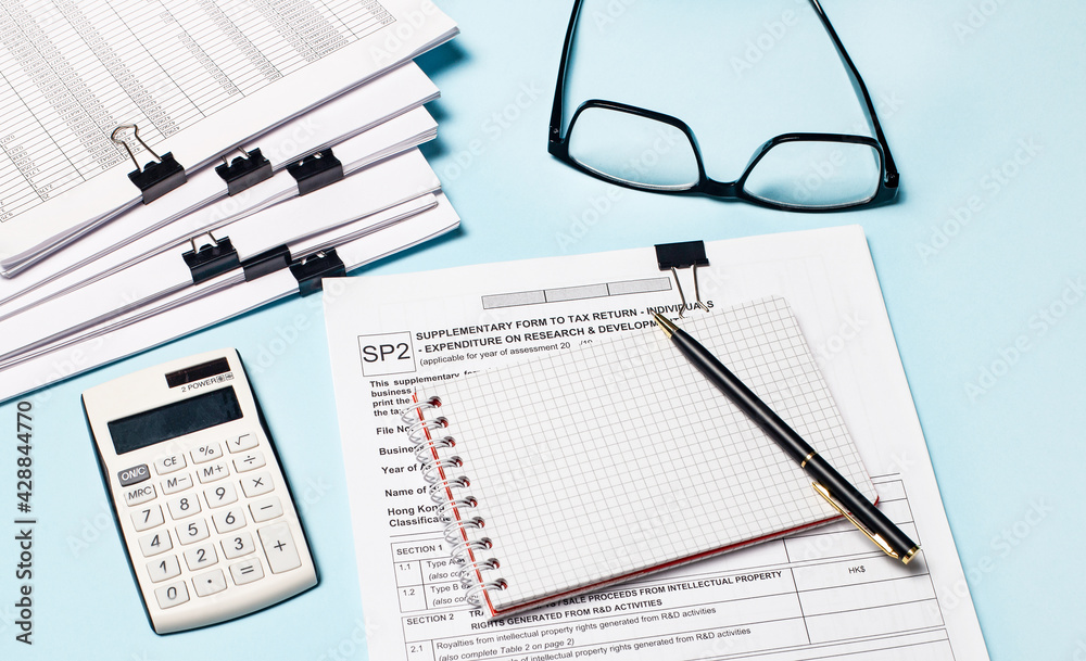 On a light blue background, there are glasses, a white calculator, documents, a notebook and a pen. Business concept On a light blue background, there are glasses, a white calculator, documents, a notebook and a pen. Business concept