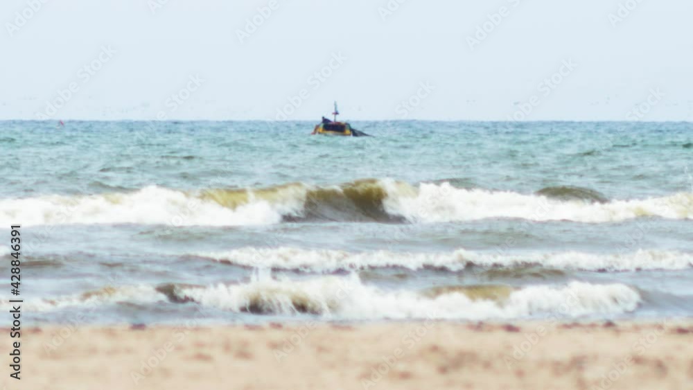Small wooden coastal fishing boat cast their nets in Baltic sea near the Liepaja (Latvia), overcast day, heat waves, white sand in foreground, low angle medium distant shot Small wooden coastal fishing boat cast their nets in Baltic sea near the Liepaja (Latvia), overcast day, heat waves, white sand in foreground, low angle medium distant shot