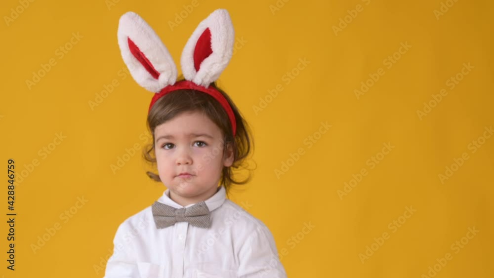 Little cute boy with rabbit ears on her head is having fun isolated on yellow studio background. Spring holiday concept Little cute boy with rabbit ears on her head is having fun isolated on yellow studio background. Spring holiday concept