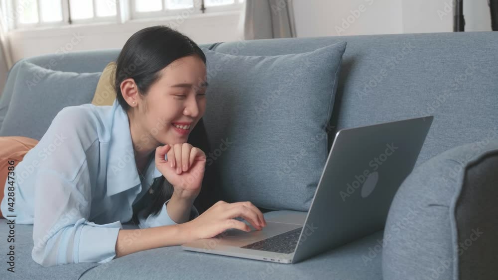 Female Lying On A Sofa And Using Laptop In Living Room Female Lying On A Sofa And Using Laptop In Living Room