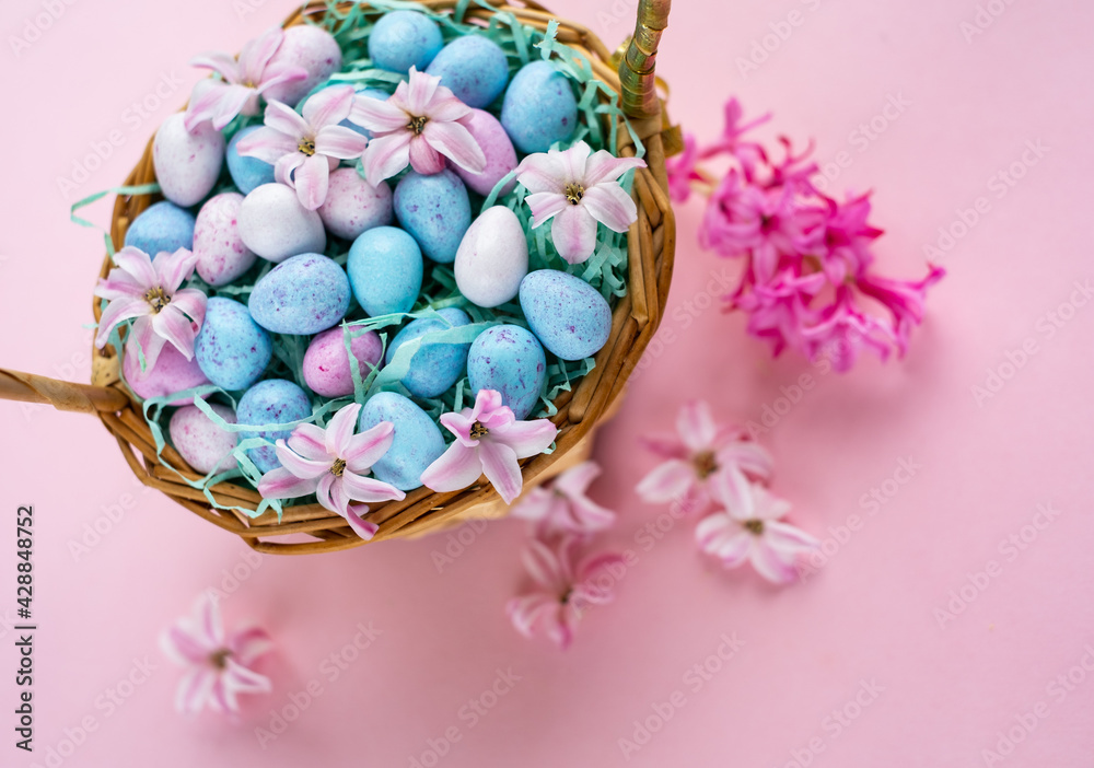 Happy Easter. Wicker basket with chocolat eggs and spring bright flowers, selective focus