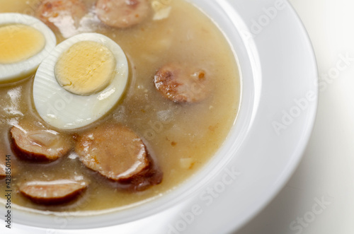 Traditional polish sour soup with sausage and eggs in a white deep plate
