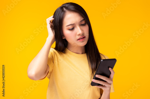 Beautiful young woman get confused and frustrated of application shopping online Girl hold mobile phone, look at cellphone with expression face She get disappointed of broken phone yellow background