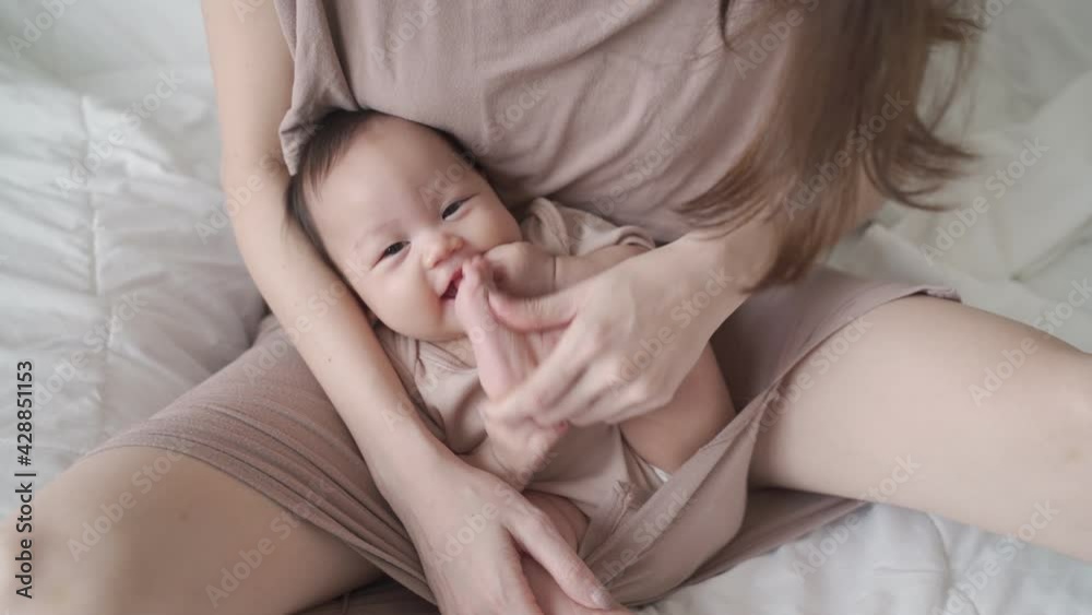 asian mother parent playing with baby infant enjoy sucking hand fingers and foot. kid laughing when play with mom on bed in bedroom. life at home. happy newborn baby learning development skill lesson. asian mother parent playing with baby infant enjoy sucking hand fingers and foot. kid laughing when play with mom on bed in bedroom. life at home. happy newborn baby learning development skill lesson.