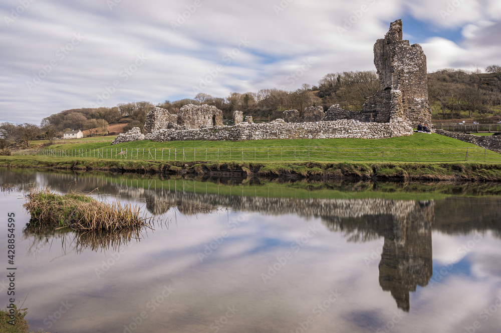 Ogmore Castle, A ruined Norman castle near Bridgend, south Wales.  The castle is reflected on the smooth water of the river Ogmore.