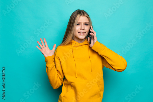 Young woman talking on mobile phone posing isolated on turquoise background.