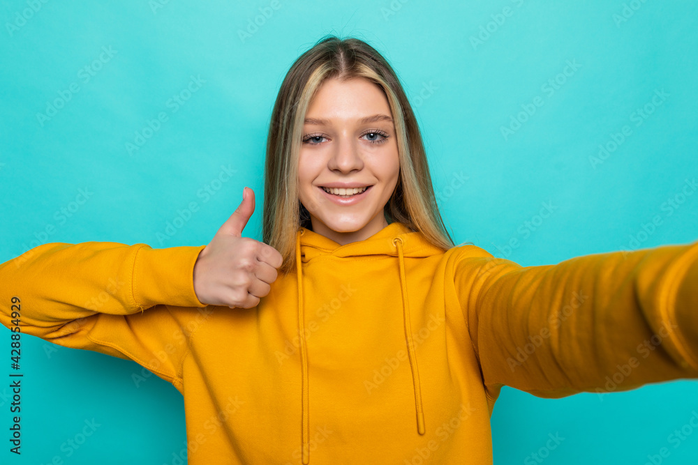 Young woman with thumb up take selfie on turquoise color background Young woman with thumb up take selfie on turquoise color background
