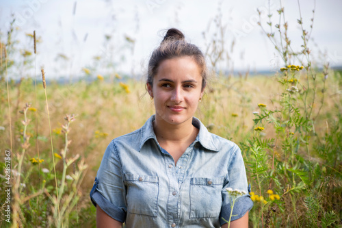 beautiful young woman sits in a meadow in flowers on a sunny summer day and smiles.