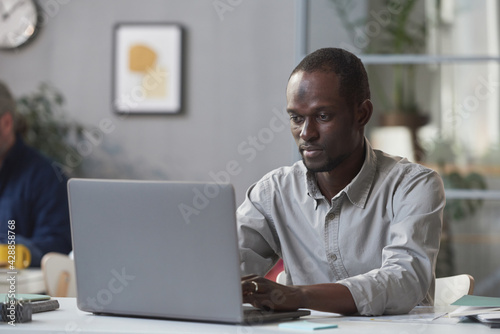 African young businessman sitting at his workplace and typing on laptop at office