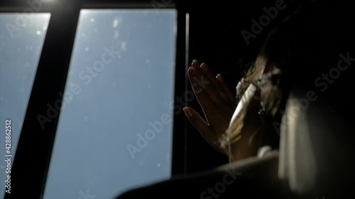 girl in a dark room covers the sun with her hand