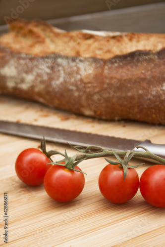 Fresh colorful cherry tomatoes on wooden table. Freshly baked bread and metallic knife on background.