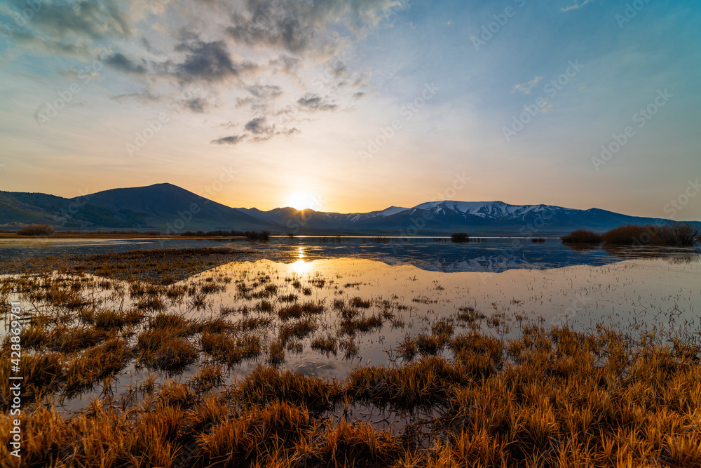 Beautiful bright sunrise over the lake and mountains, reflection in the water. Panoramic view.