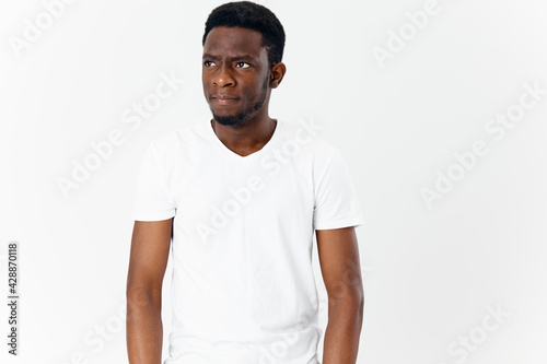  African guy in a white T-shirt looks to the side on a light background