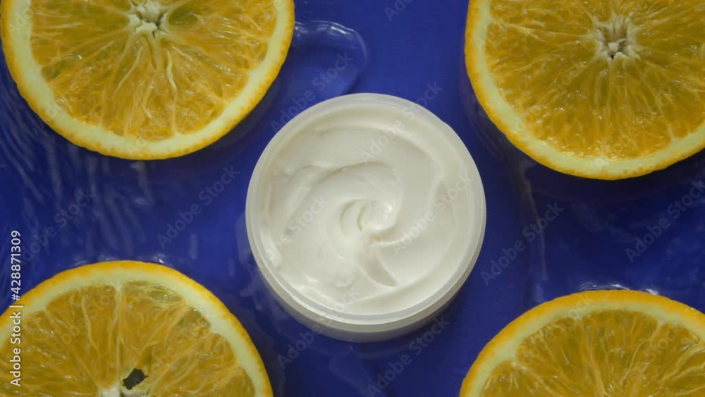 Cosmetic jar with moisturizing cream and fresh citrus fruits in clean water splash on blue background. Top view. Skin care products, natural ingredients, simple skin routines, beauty, fresh concept Cosmetic jar with moisturizing cream and fresh citrus fruits in clean water splash on blue background. Top view. Skin care products, natural ingredients, simple skin routines, beauty, fresh concept