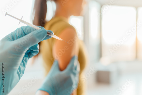 COVID-19 Coronavirus vaccine shot given by doctor or nurse at hospital healthcare clinic to middle aged woman patient. Closeup of syringe needle ready to be given in arm.