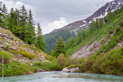 Walk to Lake Combal. Landscape at the Miage glacier, with the view of the river and the mountains, in summer, with cloudy sky. Italian Alps. Valle d'Aosta. Italy