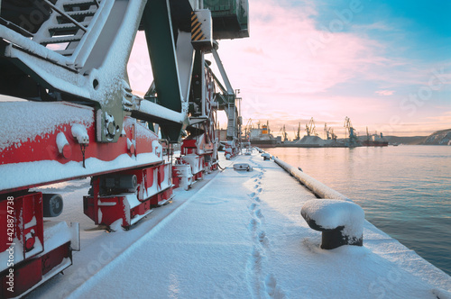 Snow, Morning at the seaport, mooring bollard at the mooring wall, portal cranes