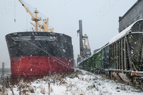 Autumn bad weather, snowfall, bulk carrier at the mooring wall in the seaport. Due to the weather, loading operations were temporarily stopped. The loader is paused during snowfall.