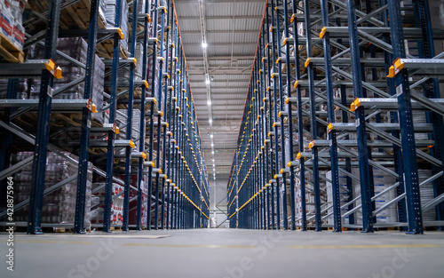 Horizontal camera move between the rows shelves with cardboard boxes and plastic packs on a palette. Logistics center interior full of racks with with large number packs.