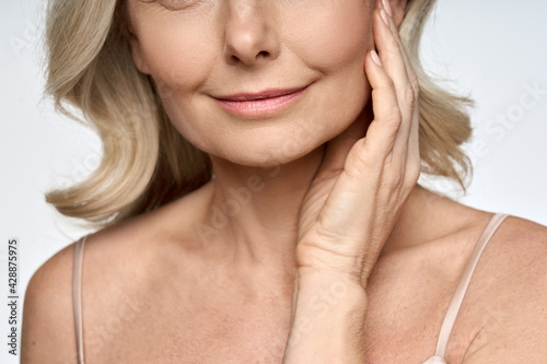 Face close up portrait of happy mid age 50 years old woman touching face with hand. Advertising of skin care anti wrinkle products for facial bottom part, lips, chin neck and decollete. photo