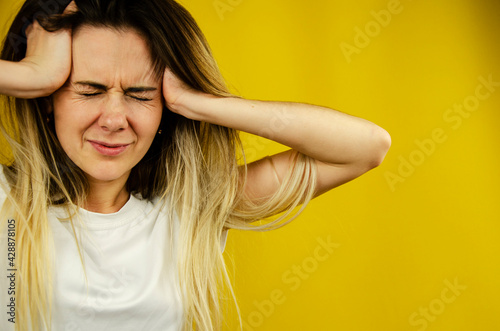 The girl clasps her head with her hands in pain. Headache. Emotional girl on a yellow background. Experience pain. Migraine. Concept. The girl is experiencing a headache. The girl is holding her head.