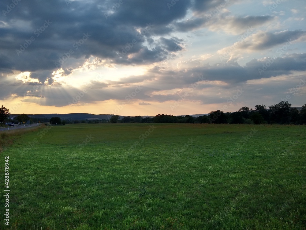 Summer Sunset with cloudy sky and green fields