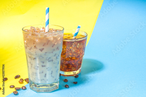 Set with different iced summer coffee drinks - espresso, frappe, latte, cappuccino, with whipped cream, syrup and crushed ice, in various glasses and mugs on trendy bright yellow blue background