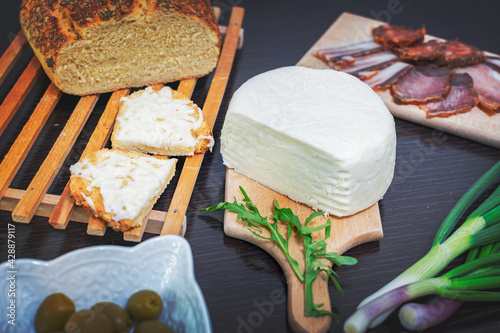 Mozzarella cheese melted on frilled bread with green onions, smoked ham, sausage, olives on a dark wooden dining table.Top view