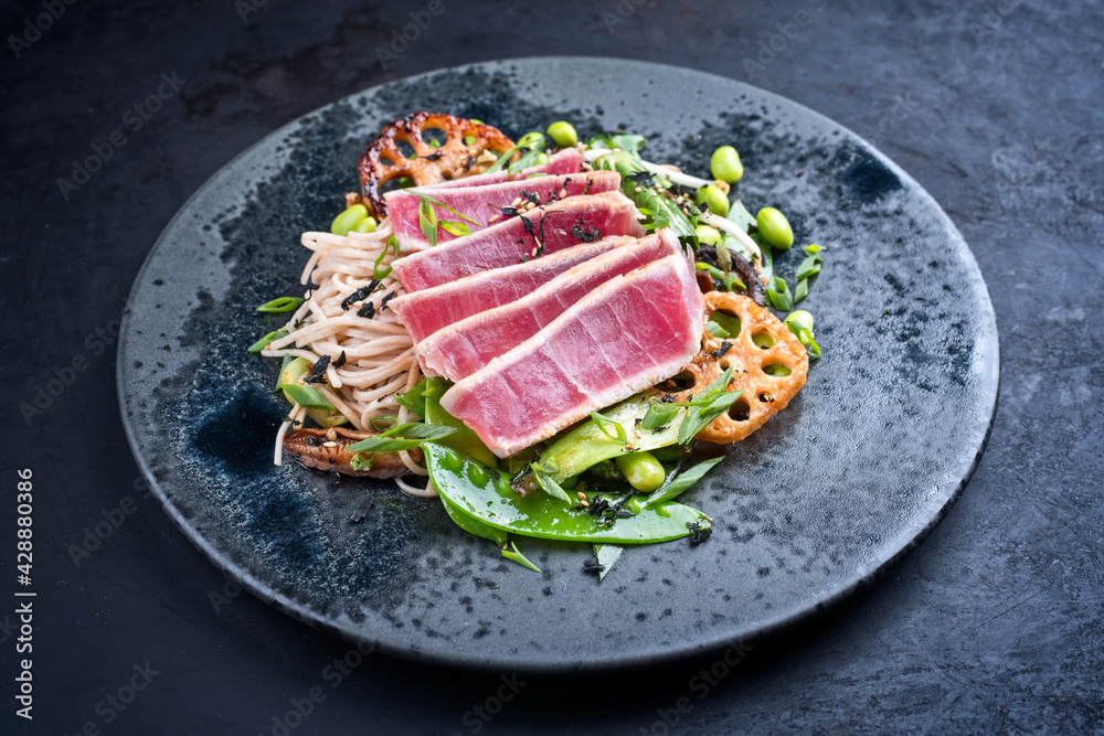 Modern style traditional Japanese gourmet seared tuna fish steak tataki with soba noodles and stir-fried vegetables served as close-up on a Nordic design plate with copy space Modern style traditional Japanese gourmet seared tuna fish steak tataki with soba noodles and stir-fried vegetables served as close-up on a Nordic design plate with copy space