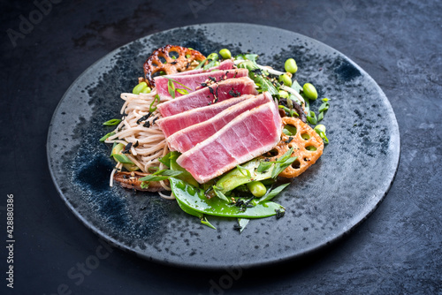 Modern style traditional Japanese gourmet seared tuna fish steak tataki with soba noodles and stir-fried vegetables served as close-up on a Nordic design plate with copy space