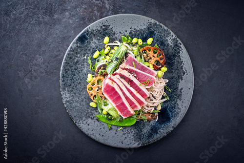 Modern style traditional Japanese gourmet seared tuna fish steak tataki with soba noodles and stir-fried vegetables served as top view on a Nordic design plate with copy space photo