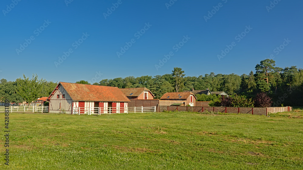 Horse stables in traditional brick stone style and meadows on a sunny day in Oise region, France, high angle view 