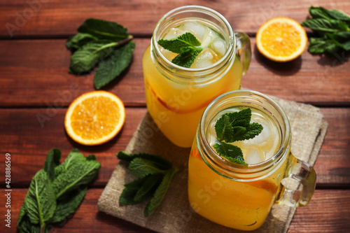 Fresh homemade citrus lemonade in jars with ice, mint and oranges on a wooden table. Summer refreshing drinks. Close-up, selective focus