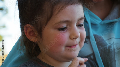 Extremly close up. Happy little dark hair and rosy cheeks girl smiling with mother browsing serfing network with mobilephone during sunset on camping vacation. Concept of nature quality family time photo