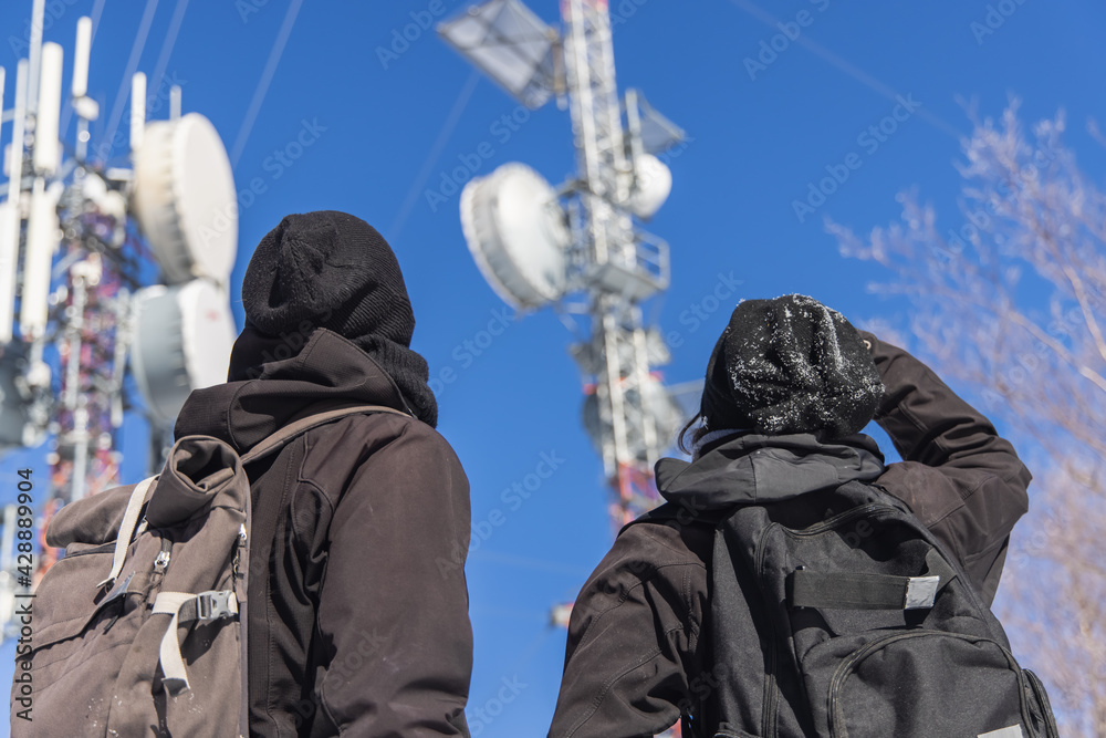 Shot of two tourists looking up at a tall infrastructure of telecommunication towers, with the attached antennas to convert signals. Shot of two tourists looking up at a tall infrastructure of telecommunication towers, with the attached antennas to convert signals.