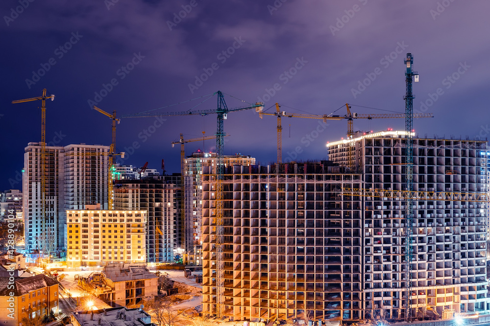 Construction site, cranes and multi-storey unfinished houses at night in winter