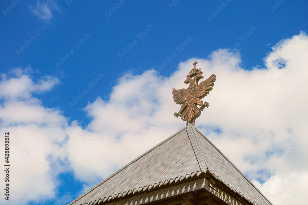 Obraz premium Wooden roof with historical coat of arms of the Russian Empire under blue sky. Ancient fortress roofing architecture.