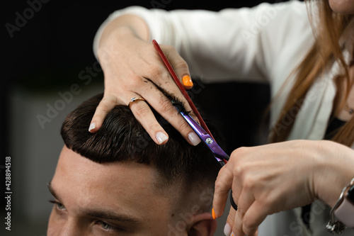 Haircut and styling in barbershop for handsome man. Woman making hairstyle using scissors.