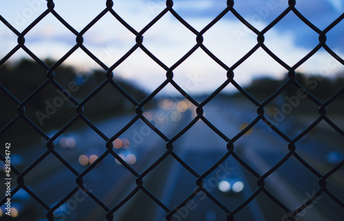 Chain link fence over dark highway with some headlights in background