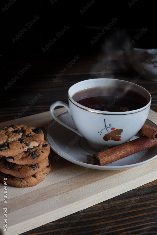 A cup of aromatic black coffee, grains of different varieties on the table and cinnamon sticks and chocolate chip cookies. Morning espresso or Americano coffee for breakfast in a beautiful cup. A cup of aromatic black coffee, grains of different varieties on the table and cinnamon sticks and chocolate chip cookies. Morning espresso or Americano coffee for breakfast in a beautiful cup.