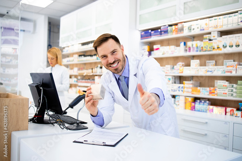 Pharmacist selling medicines in drug store and holding thumbs up.