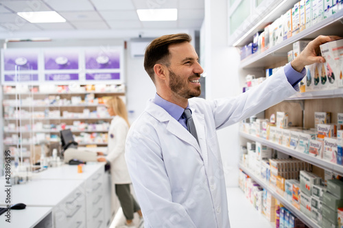 Pharmacist working in pharmacy store and arranging boxes of medicines on the shelf.